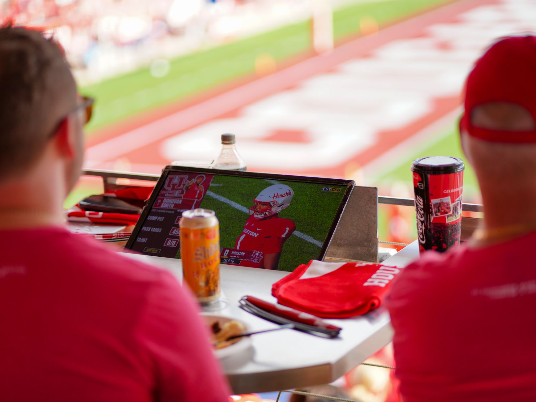 College football fans in blue-and-white and red-and-black gear tailgating in a stadium parking lot before a big game, grilling food and socializing near cars and tents.