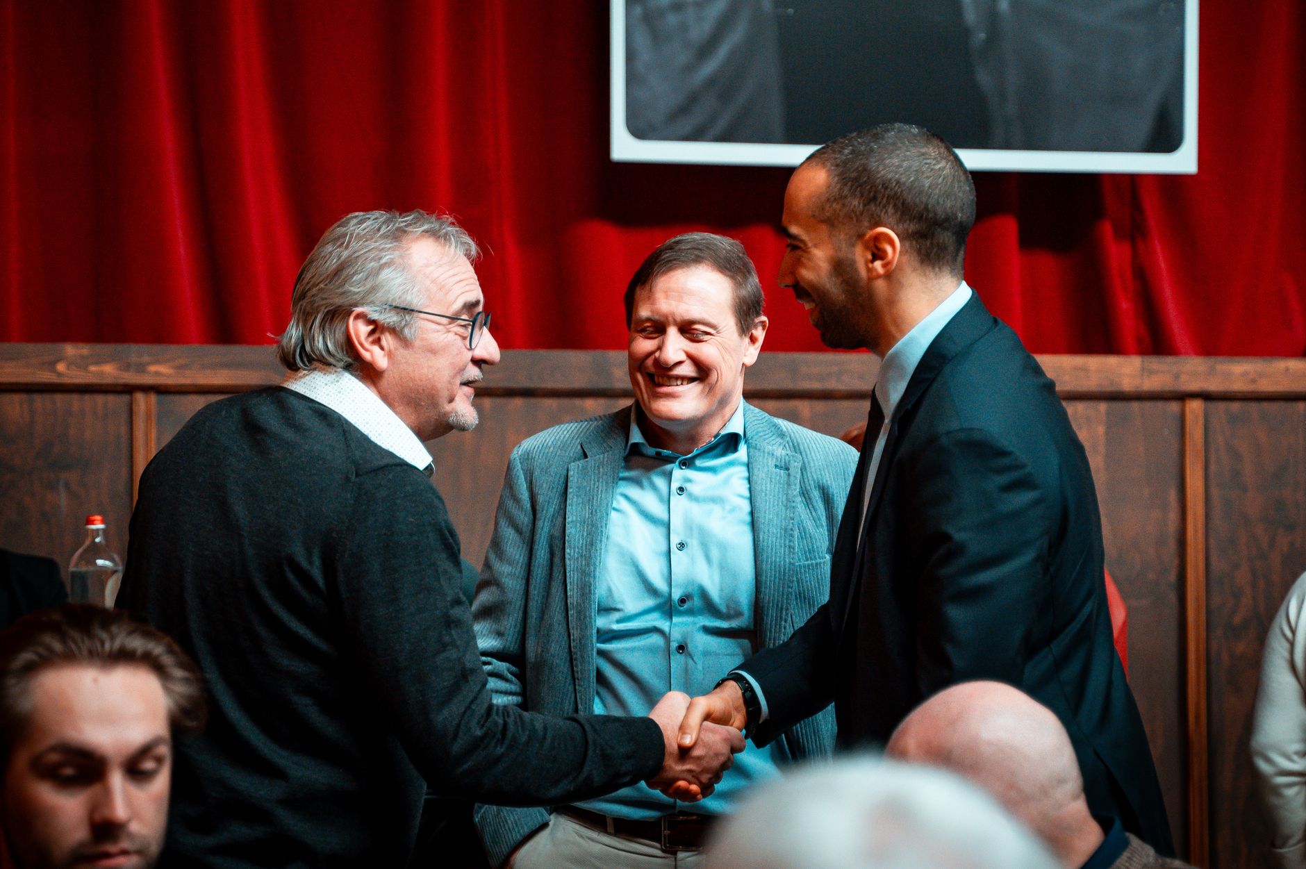 Two professionals shaking hands at a networking event while exchanging an NFC-enabled business card, showing modern digital networking.